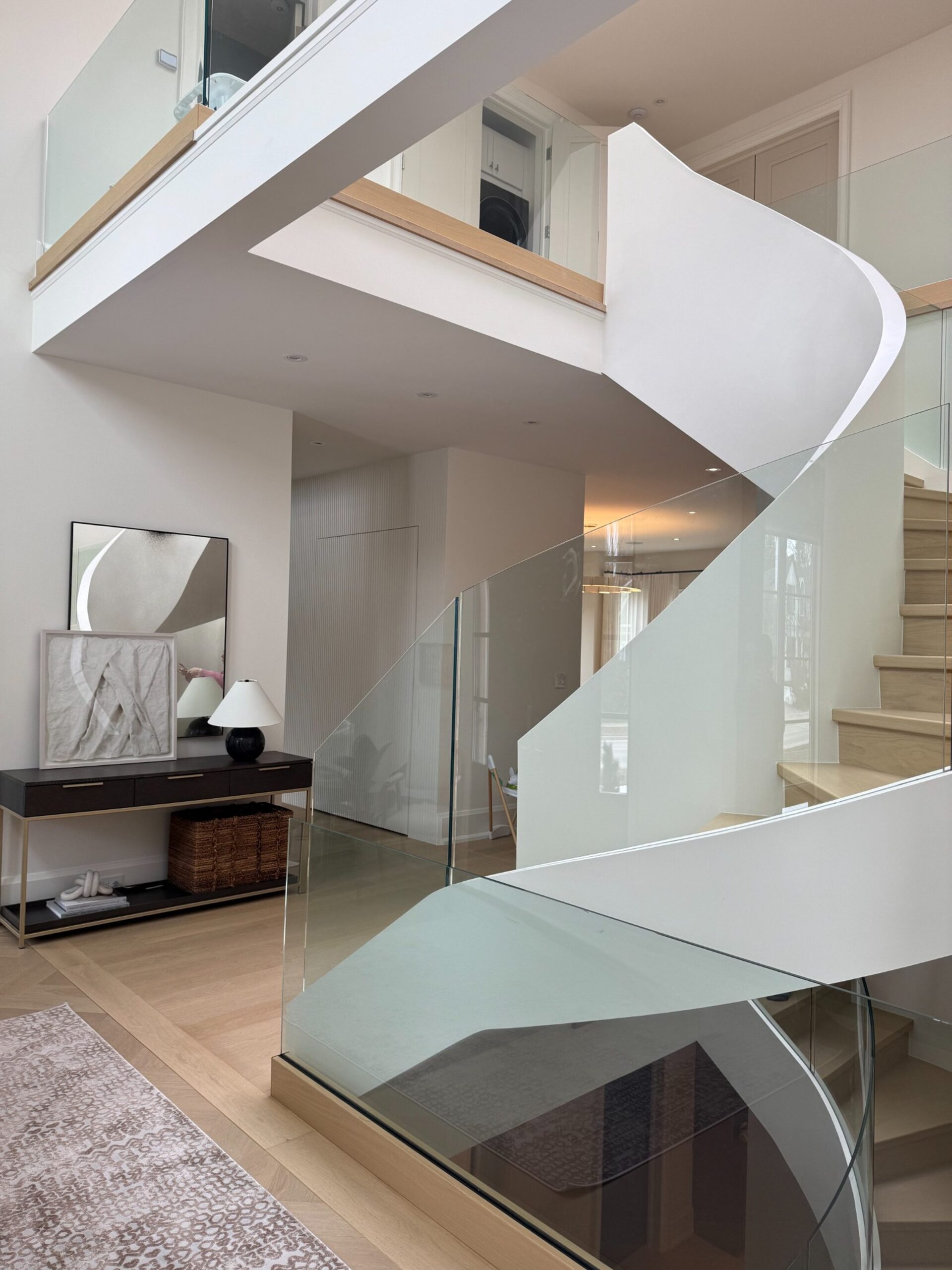 Luxury Glass Staircase | Custom Home in Oakville Luxury curved glass staircase in a custom Oakville home by Prasada Custom Homes, featuring sculpted plaster walls, floating wood treads, and glass railing