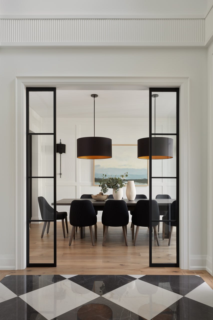 Dining room viewed through black steel-and-glass doors over a checkerboard marble floor