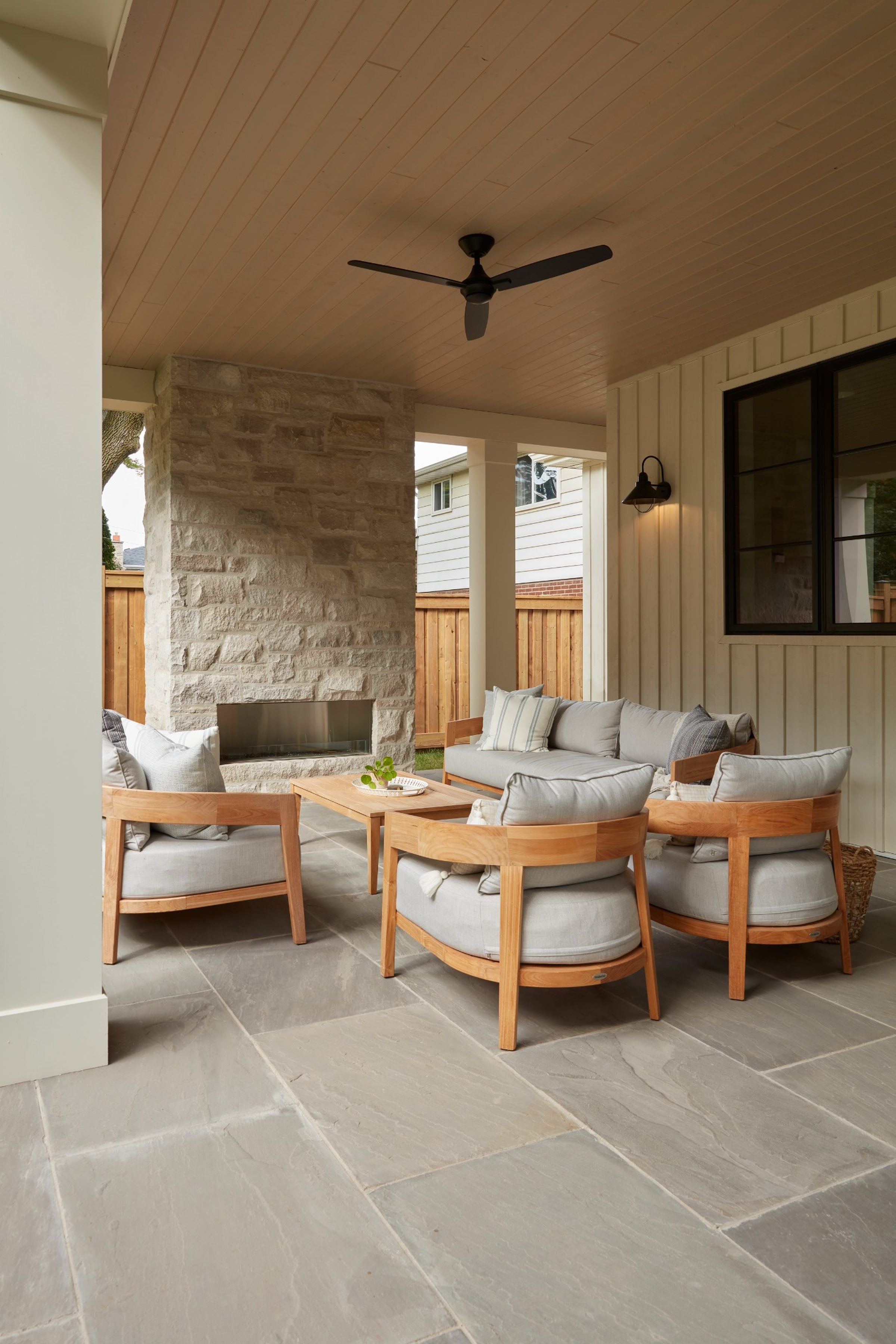 Luxury covered porch outdoor living area in a custom Oakville home by Prasada Custom Homes, featuring natural stone fireplace, wood ceiling, and refined outdoor seating