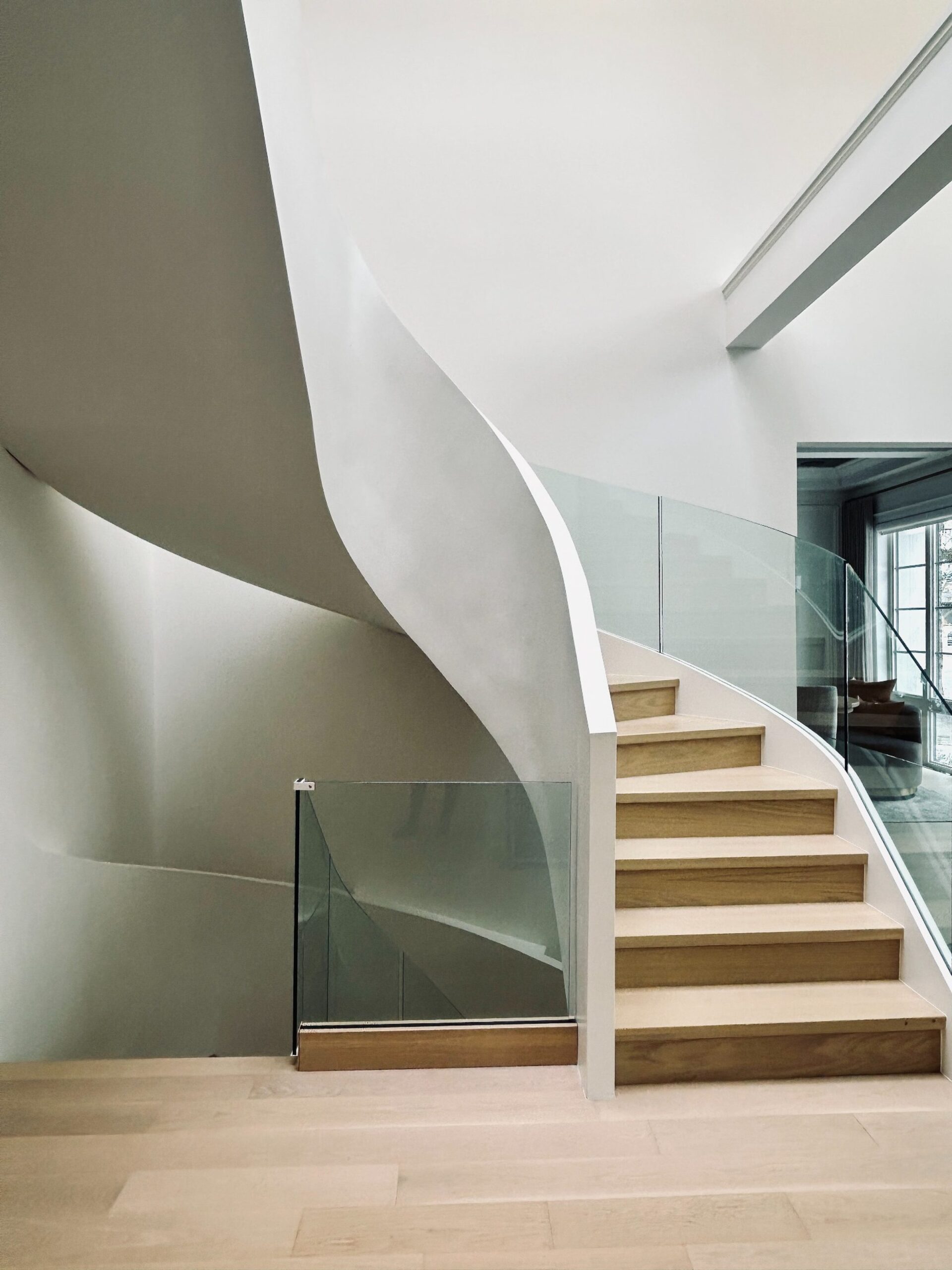 Luxury curved staircase detail in a custom Oakville home by Prasada Custom Homes, featuring sculpted plaster walls, glass railing, and wood stair treads