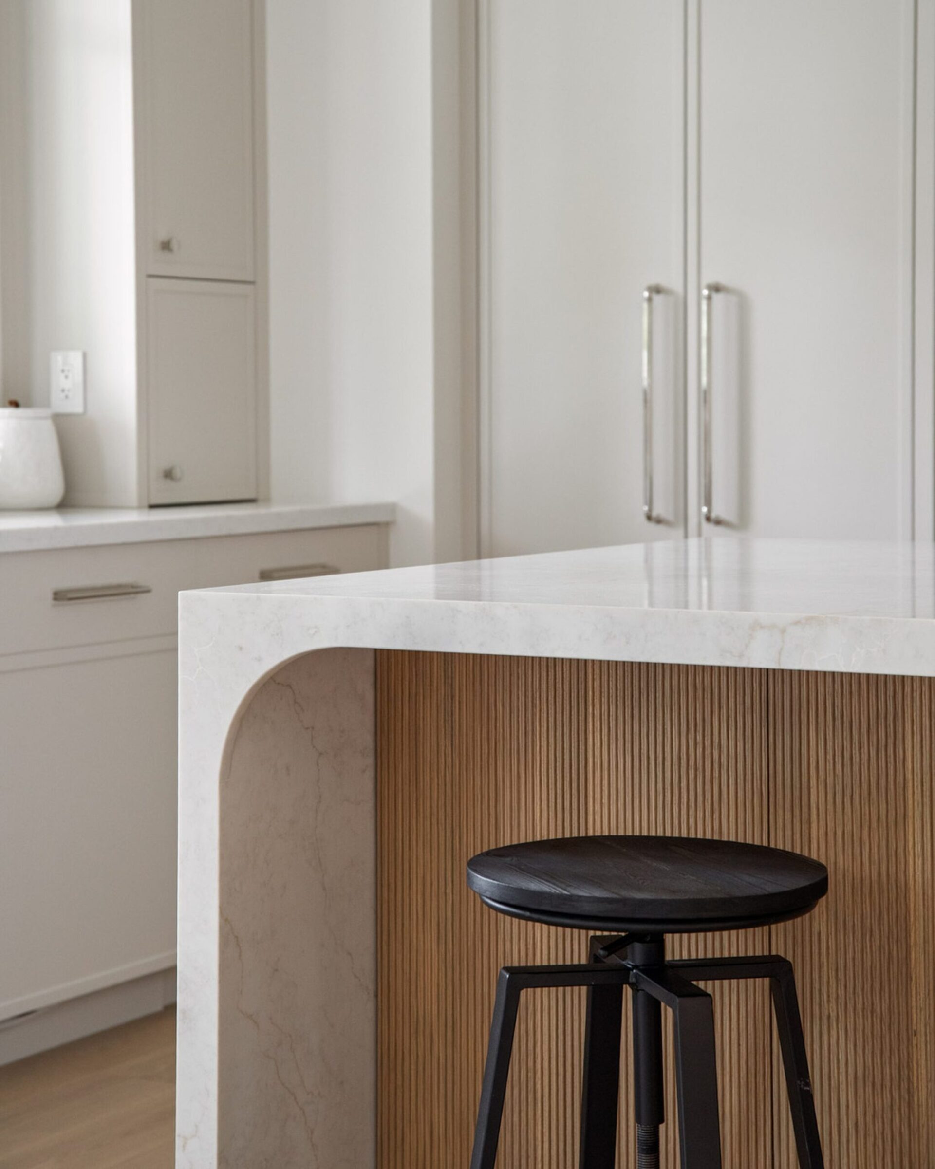 Custom kitchen island detail in a luxury Oakville home by Prasada Custom Homes, featuring stone waterfall countertop, fluted wood paneling, and refined modern design