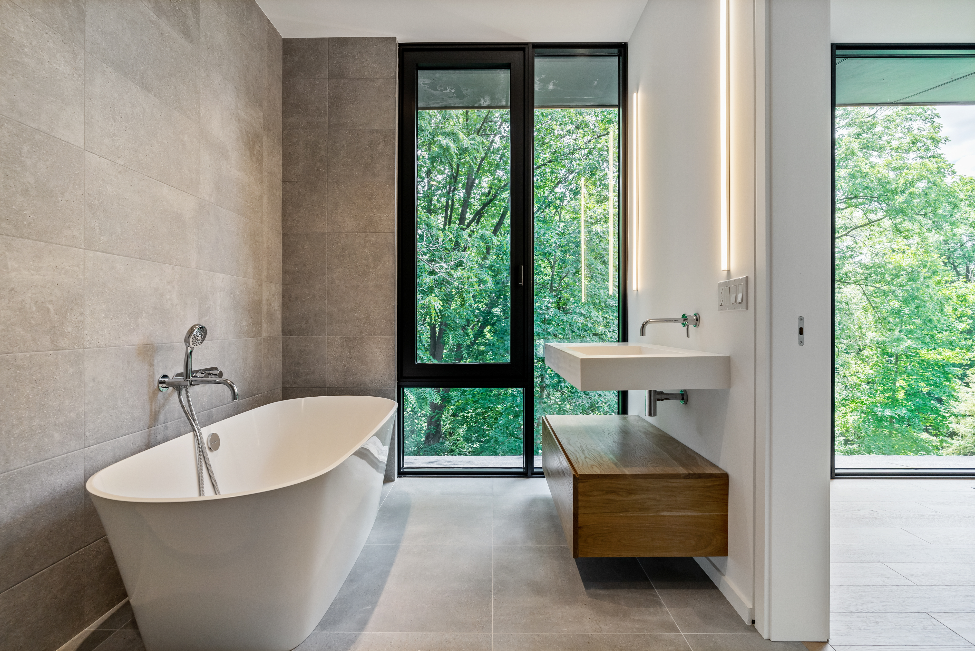 Modern primary bathroom featuring a freestanding tub, floating wood vanity, and floor-to-ceiling windows in an Oakville custom home by Prasada Custom Homes