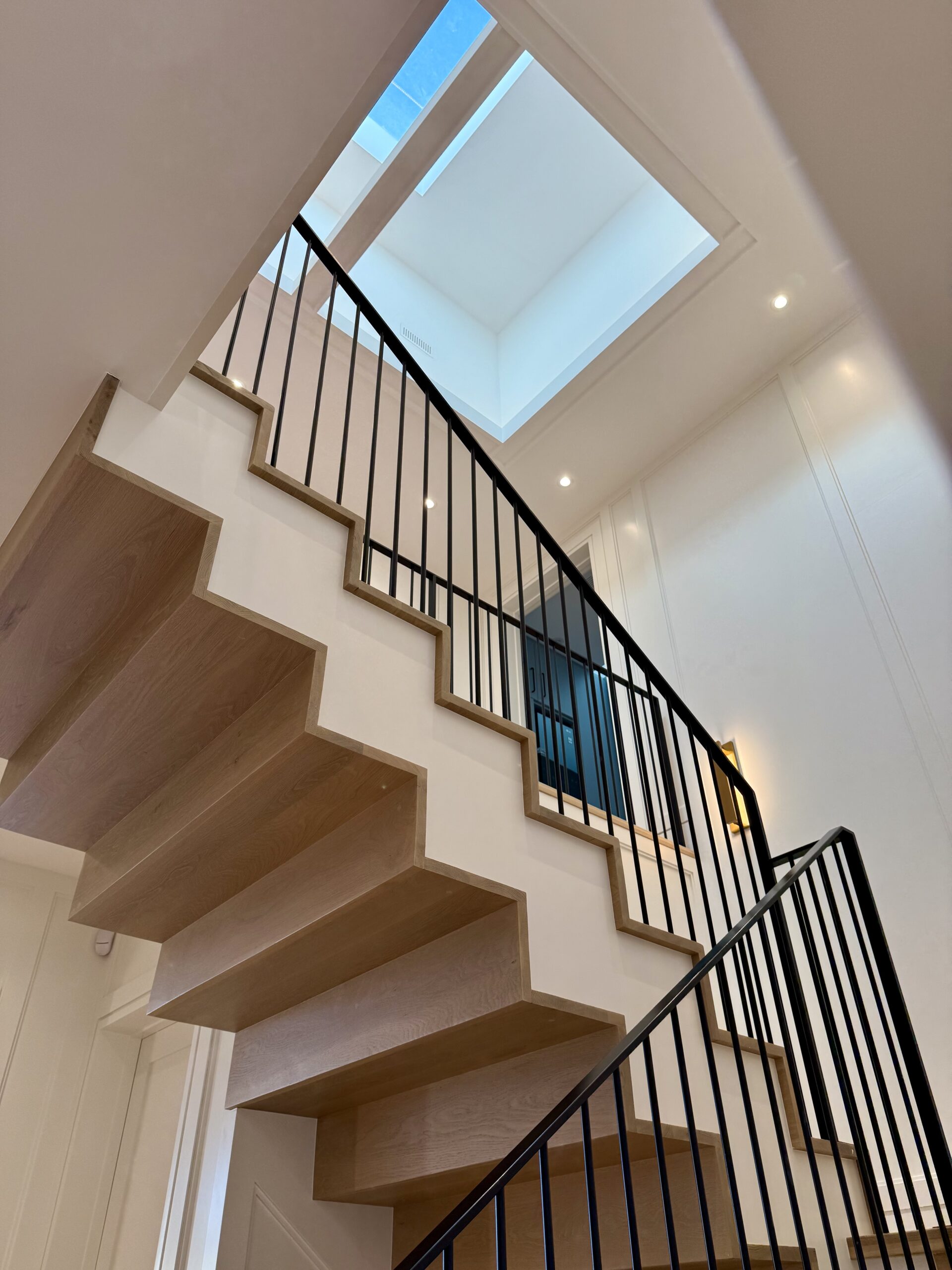 Modern floating staircase with skylight in a custom Oakville home by Prasada Custom Homes, featuring wood treads, black railing, and clean architectural detailing