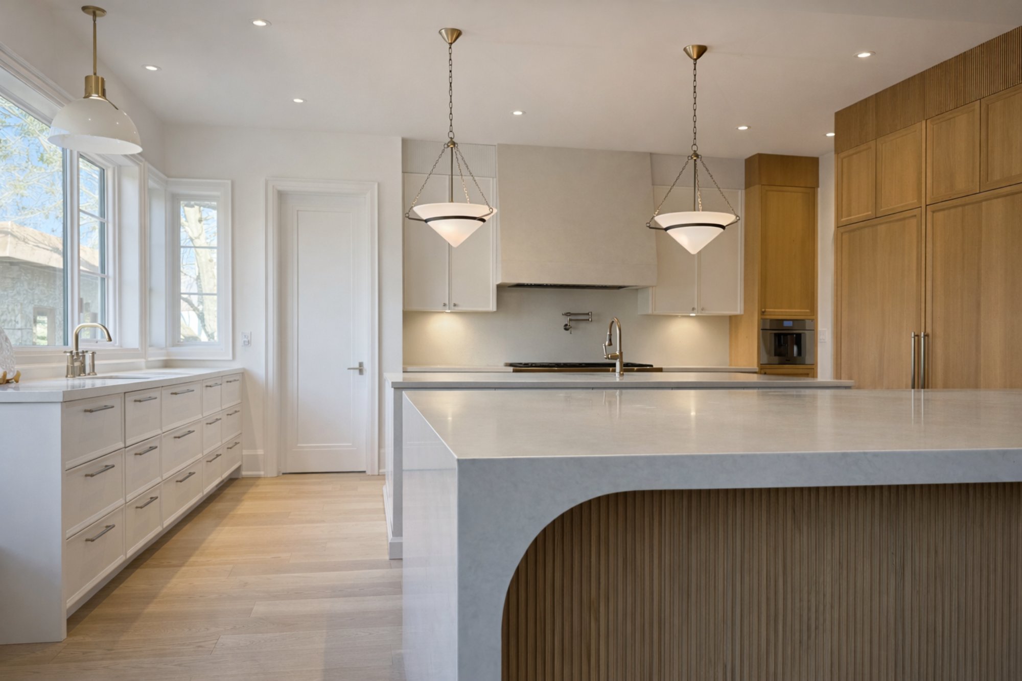 Luxury custom kitchen in Oakville featuring a curved waterfall island, marble countertops, custom wood millwork, and designer pendant lighting by Prasada Custom Homes